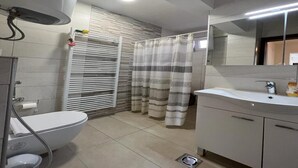Un baño moderno con inodoro, bidé, tocador con espejo y cortina de ducha.
