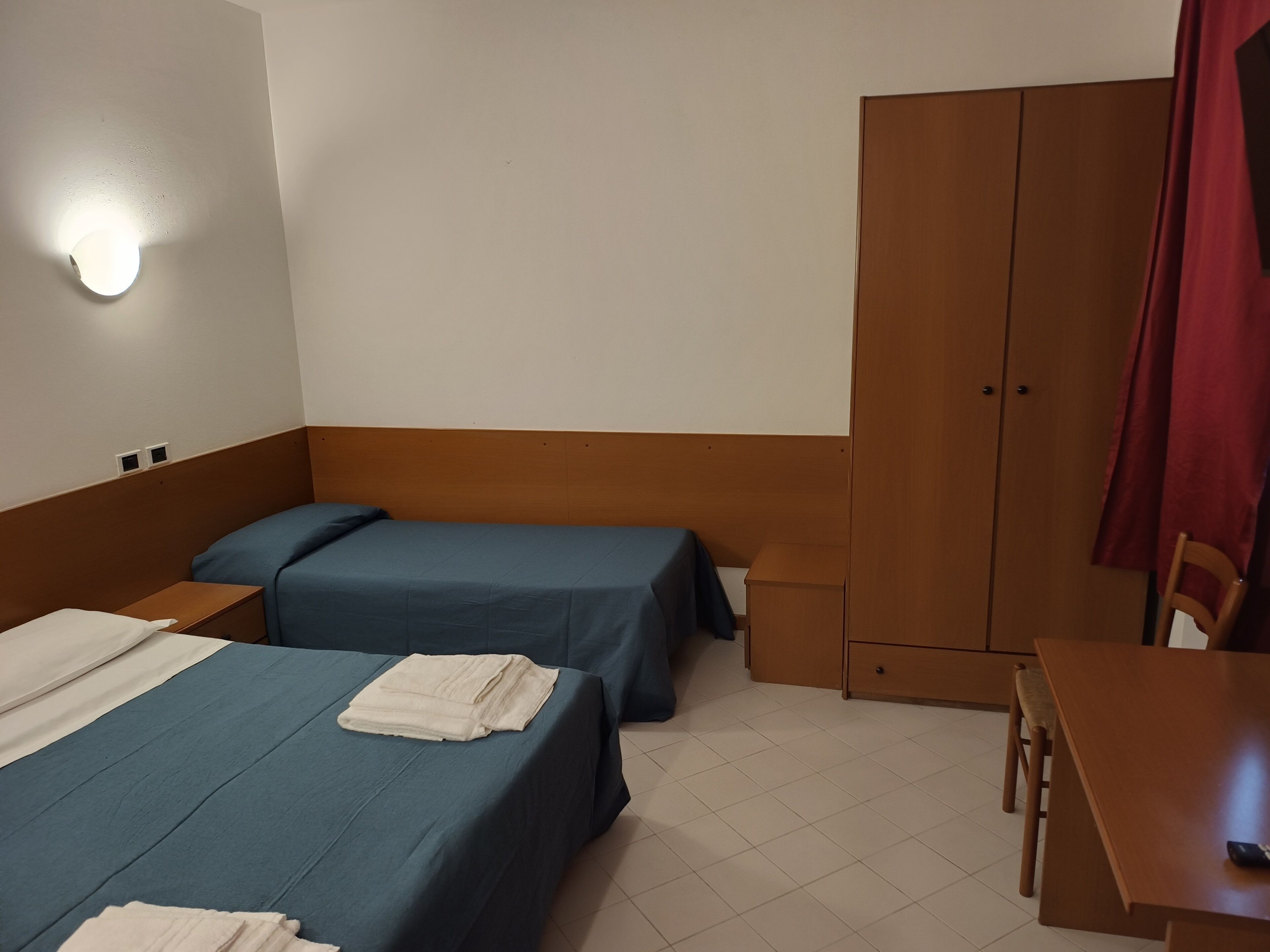 Een hotelkamer met twee bedden, een houten kledingkast, een tafeltje en een stoel.