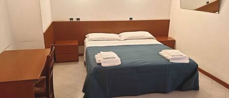 Quarto de hotel com cama, mesas de cabeceira, escrivaninha e espelho.
