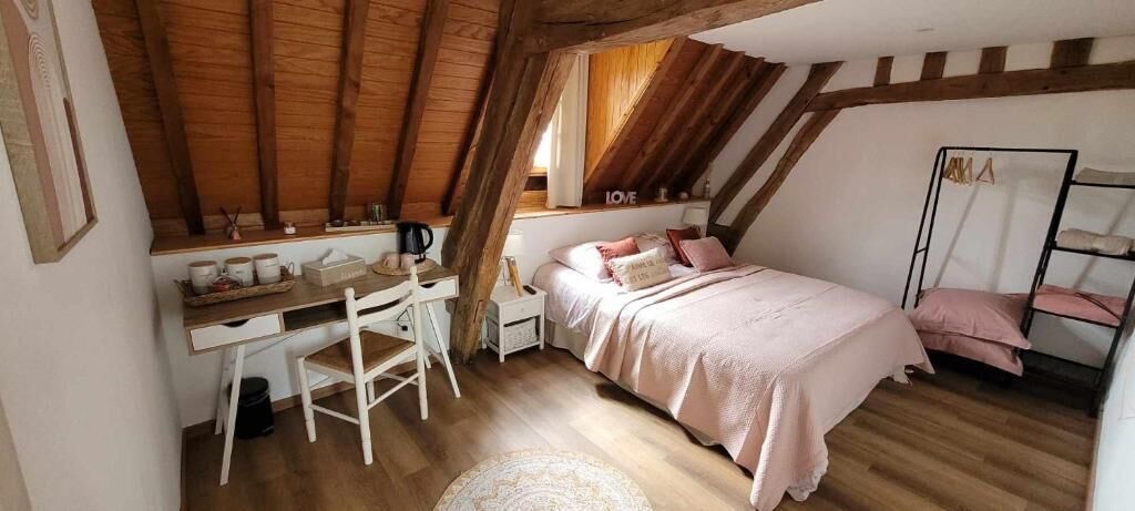 Une chambre mansardée chaleureuse, avec un bureau en bois, un lit avec une literie rose et une fenêtre offrant une belle vue.