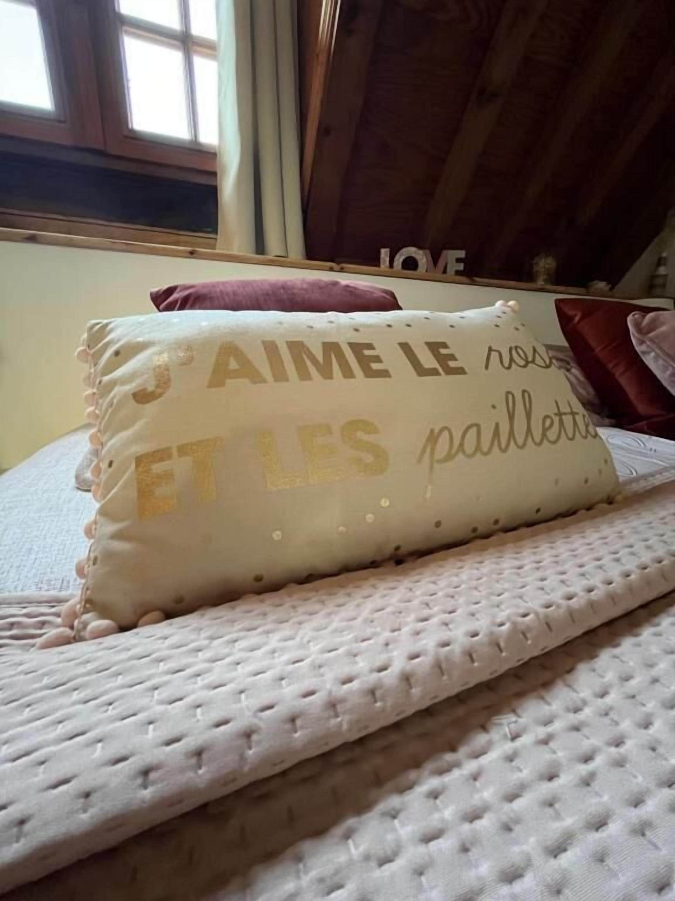 A bed with a textured white mattress and a pillow with the text "AIME LE roses ET LES paillottes".