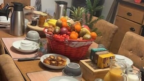 Una mesa de desayuno con diversos alimentos, una cafetera y una cesta de frutas.