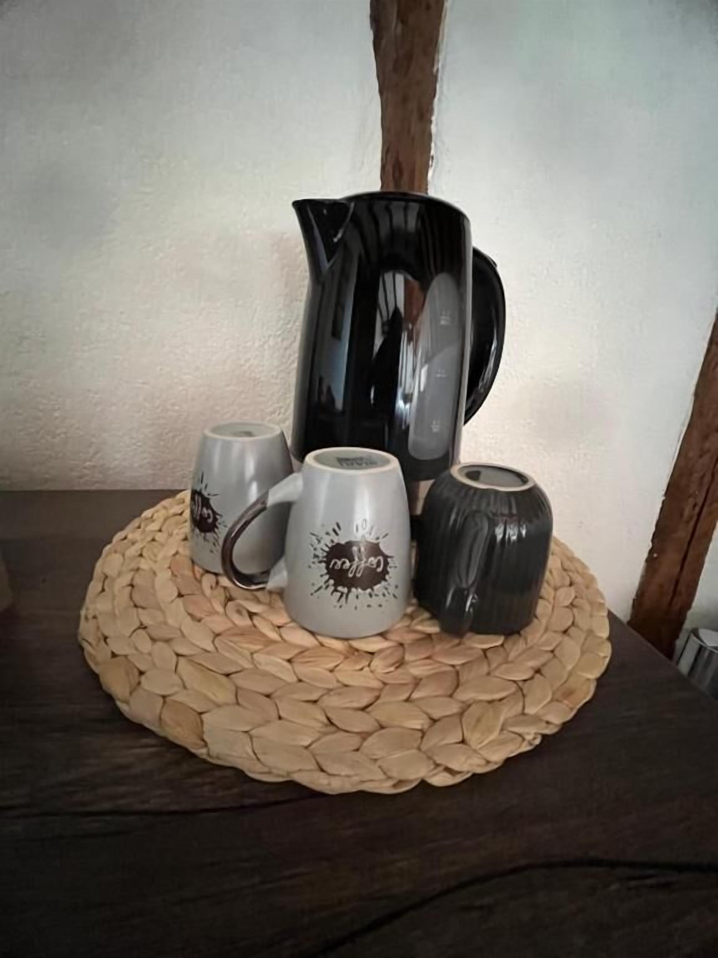 Una cafetera, dos tazas y un florero sobre un camino tejido.