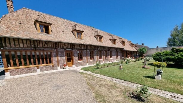 Un edificio tradicional de estructura larga y estrecha, con varias ventanas y un camino de grava que conduce a un césped bien cuidado.