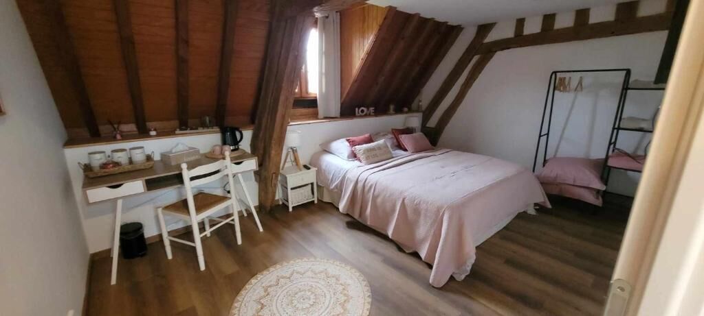 Un dormitorio con techo inclinado, una cama con ropa de cama rosa, un escritorio con una silla y una ventana pequeña.