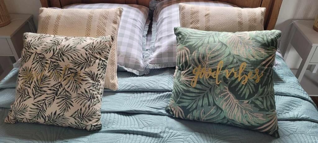 Una cama con un edredón azul y dos almohadas decorativas con diseños de hojas y texto.