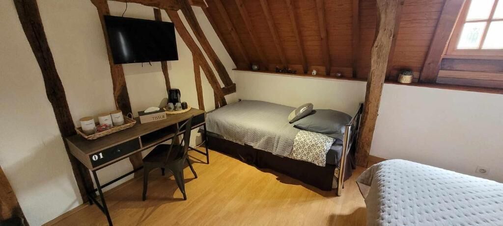 Een slaapkamer met een enkel bed, een bureau met stoel, een aan de muur bevestigde televisie en een raam met uitzicht op de omgeving.
