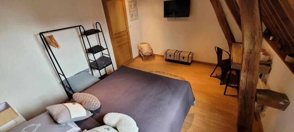 A bedroom with a bed, a wooden chair, a small table, and a TV mounted on the wall.