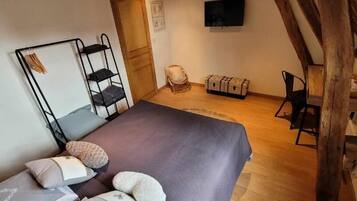 A bedroom with a bed, a wooden chair, a small table, and a TV mounted on the wall.