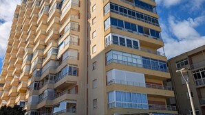 Un edificio residencial de varios pisos con balcones, una entrada porticada y un cielo despejado.