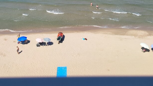 Een strand met helderblauw water, een zandstrand en enkele parasols en ligbedden.