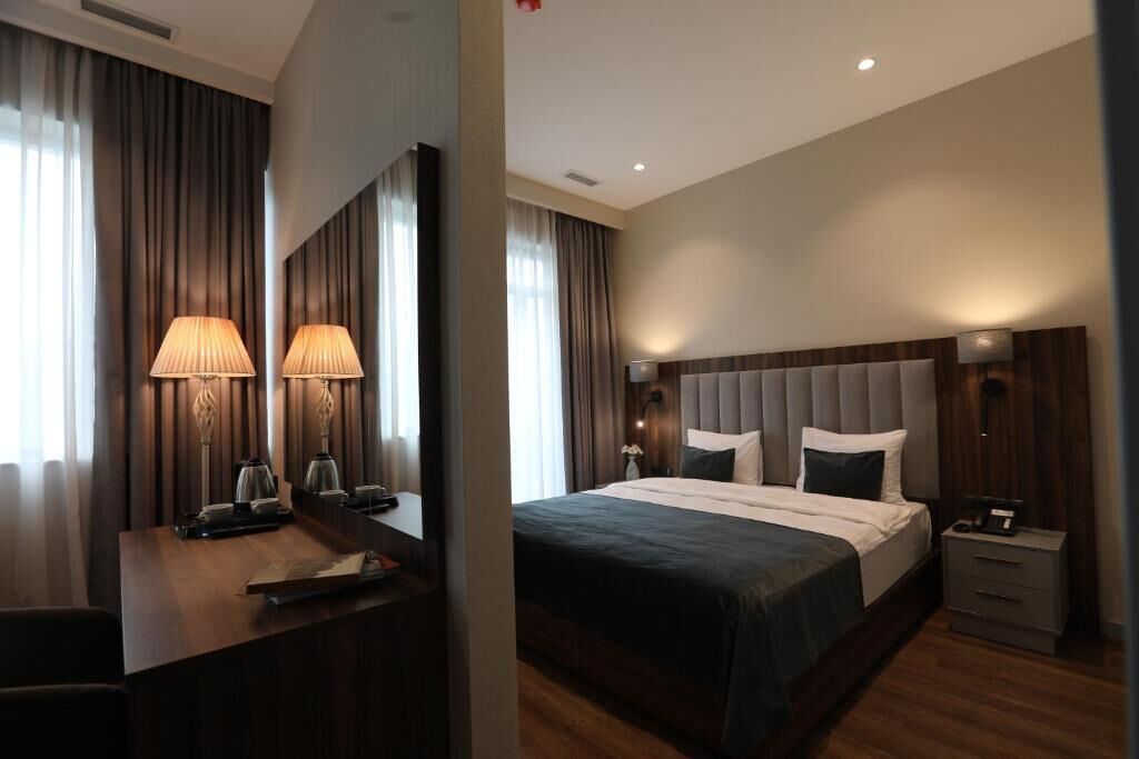 Una habitación de hotel moderna con una cama grande, un escritorio con lámparas y una mesita de noche.