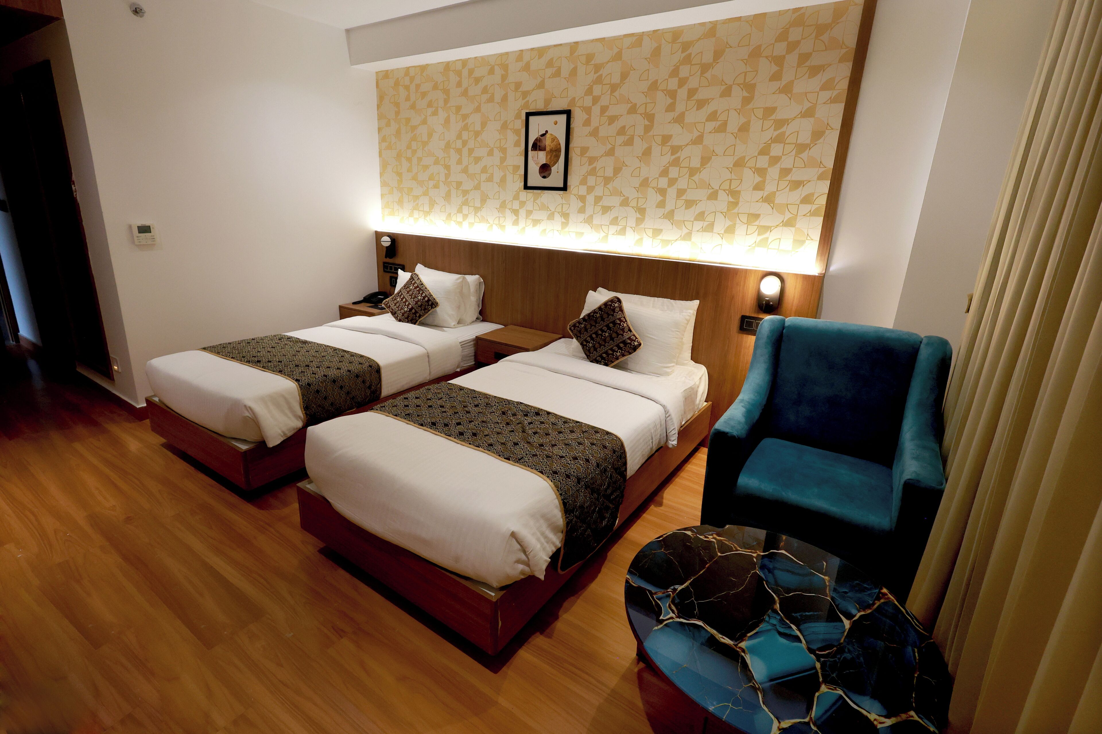 A hotel room with two beds, a blue armchair, and a patterned wall.