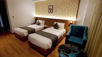 A hotel room with two beds, a blue armchair, and a patterned wall.