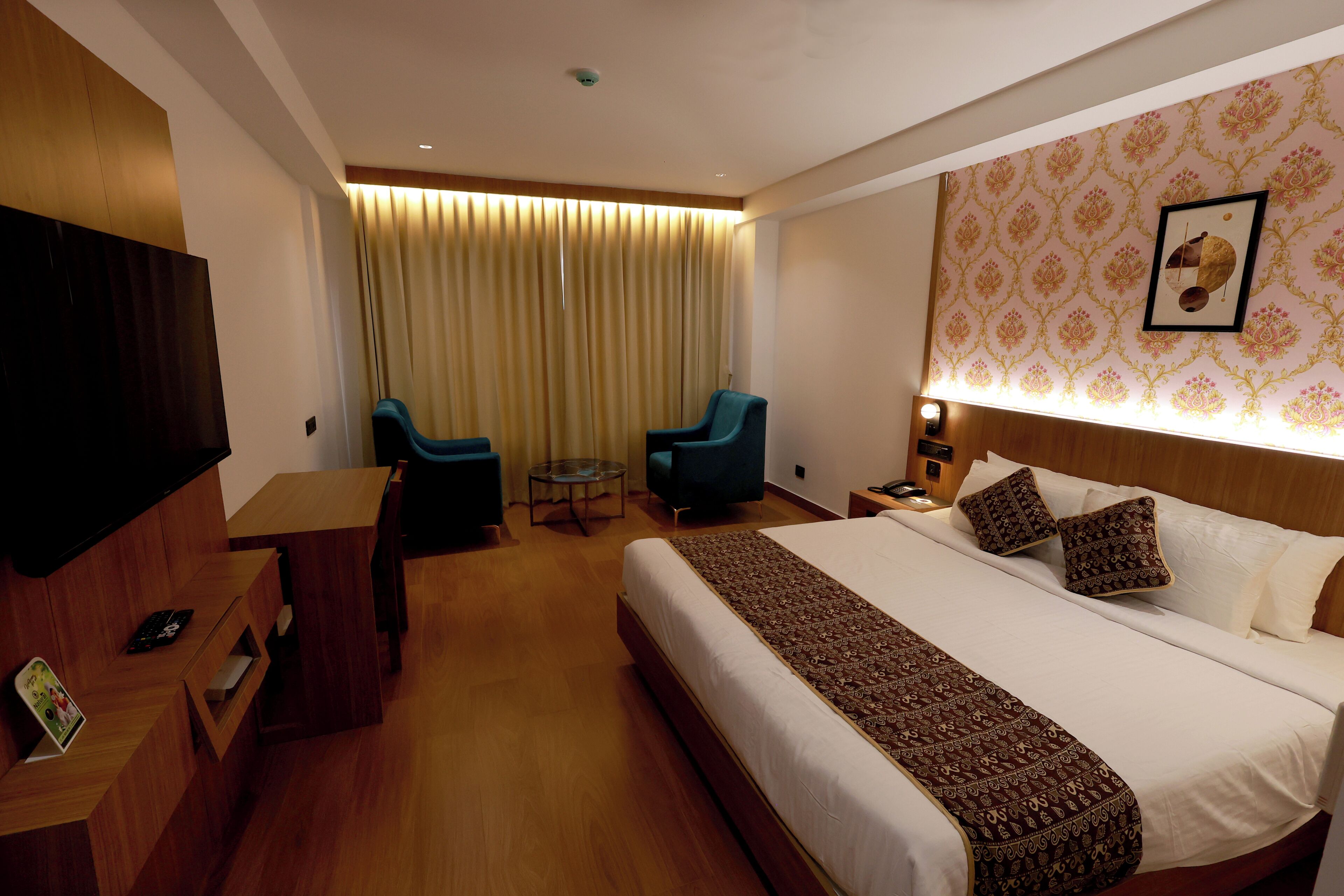 Habitación de hotel con una cama grande, dos sillones, una mesita, un televisor y un cuadro colgado en la pared.