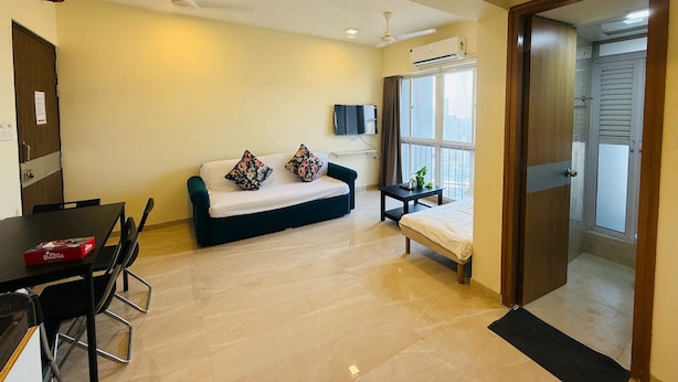 A living room with a sofa, a coffee table, and a TV mounted on the wall. - 1BR Service Apart Parel 3701 Near TMH By Florastays (Mumbai)