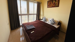 A hotel room with a large bed, a painting on the wall, and a view of the city through the window. - 1BR Service Apart Parel 3701 Near TMH By Florastays (Mumbai)
