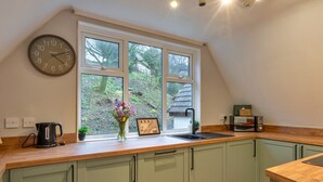 A kitchen with a wooden countertop, a sink, a clock, and a window with a view of trees and a house. - Toblerone Lodge (Callington)