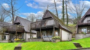 A row of wooden cottages with sloped roofs and balconies, set on a grassy hillside with a clear sky. - Toblerone Lodge (Callington)
