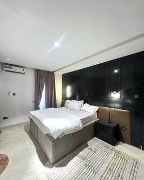 A modern bedroom with a large bed, a bedside table, a wardrobe, and an air conditioning unit. - City King Hotel And Towers (Kano)