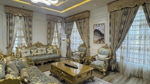 Un salon luxueux, agrémenté de meubles richement décorés, d’un grand lustre et de rideaux décoratifs.