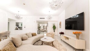 Un salon moderne avec un canapé d’angle, une table basse ronde, un téléviseur fixé au mur et une console minimaliste agrémentée d’un vase de fleurs.