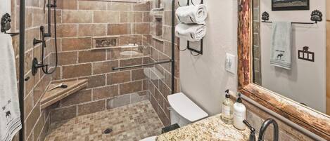 Un baño con ducha envuelta en vidrio, inodoro blanco y encimera de granito con lavabo y grifo.