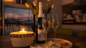A table with a bottle of wine, two glasses, a candle, and tulips. - ÖKO houseboat Morgenrot with sun terrace & harbor view near Stralsund (Stralsund)