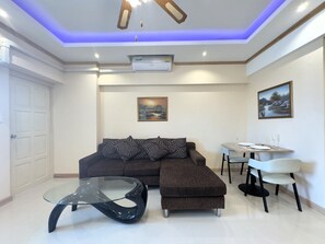 Ein modernes Wohnzimmer mit einem Ecksofa, einem Glastisch und einem Essbereich mit kleinem Tisch und Stühlen.