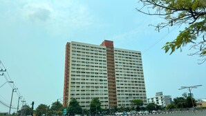 A multi-story building with a prominent red and beige facade, surrounded by a parking lot with vehicles and a red and white barrier gate. - Stylish 1-bedroom Corner Condo Near Thepprasit Night Market -keha Condominium (Pattaya)