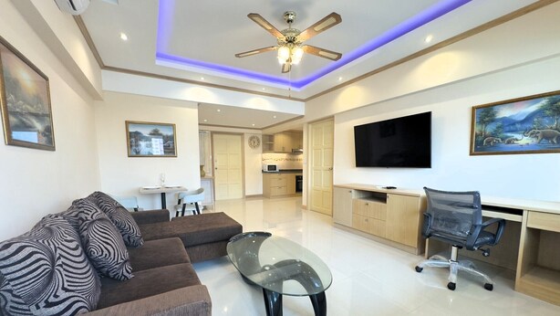 A modern living room with a sofa, glass coffee table, and a TV. - Stylish 1-bedroom Corner Condo Near Thepprasit Night Market -keha Condominium (Pattaya)