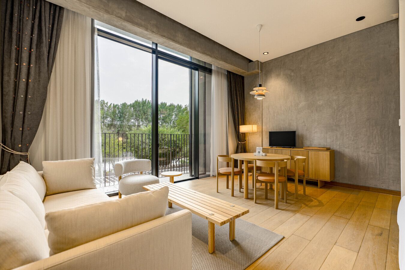 Un salon moderne comprenant un canapé, des fauteuils, une table à manger, un téléviseur et un balcon avec vue sur les arbres.