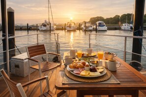 Ein Esstisch mit Speisen und Getränken auf einer Terrasse mit Blick auf eine Marina und Boote.