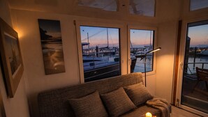 Um quarto aconchegante com sofá, mesa com velas e vista para barcos através de grandes janelas.