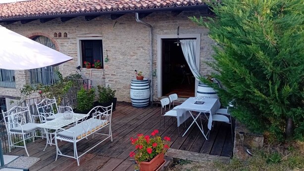 An outdoor patio with white metal furniture, a stone building with a tiled roof, and potted plants.