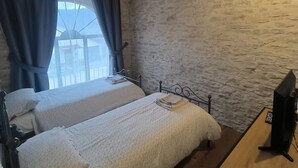 A bedroom with two beds, a wooden desk, and a stone wall.