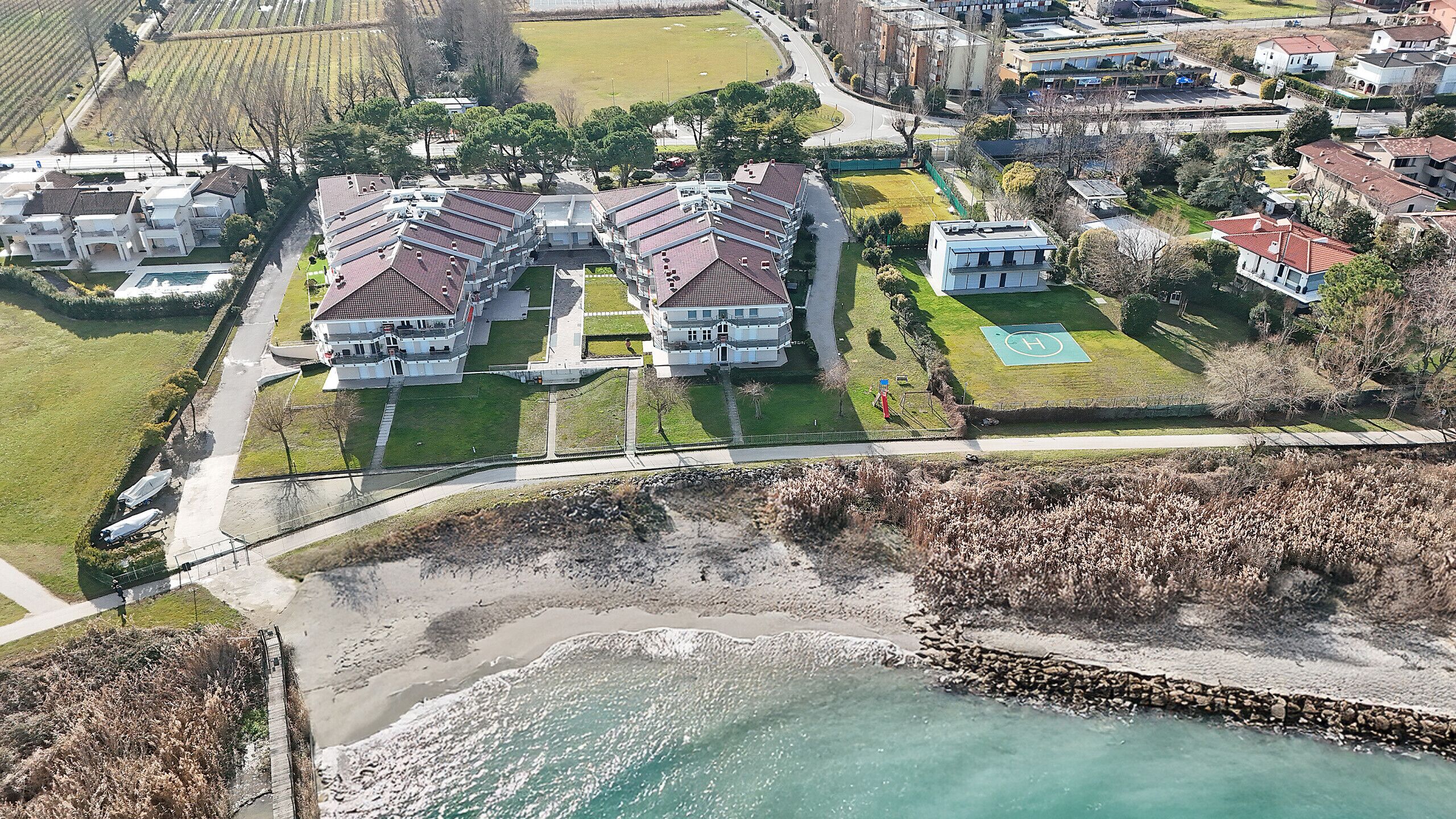 An aerial view of a coastal residential area with multiple two-story houses, a beach, and a road.
