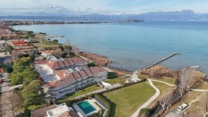An aerial view of a residential area with a large building, a swimming pool, and a dock extending into a lake. - Sunset on Sirmione in Sirmione (Sirmione)