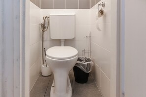 Ein kleines, sauberes Badezimmer mit Toilette, Mülleimer und Duschschlauch.