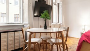 Ein Essbereich mit einem runden Tisch, vier Stühlen, einem Blumentopf und einem an der Wand montierten Fernseher.