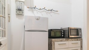 Eine kleine Küche mit einem weißen Kühlschrank, einer Mikrowelle auf einem rustikalen Holzschrank und einer Wandleuchte.