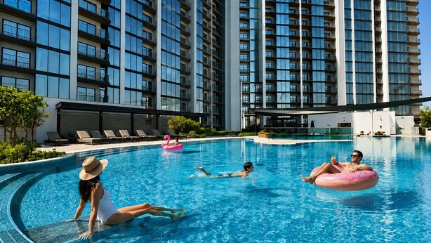Una piscina con persone, un gonfiabile a forma di fenicottero rosa e un edificio sullo sfondo con balconi.