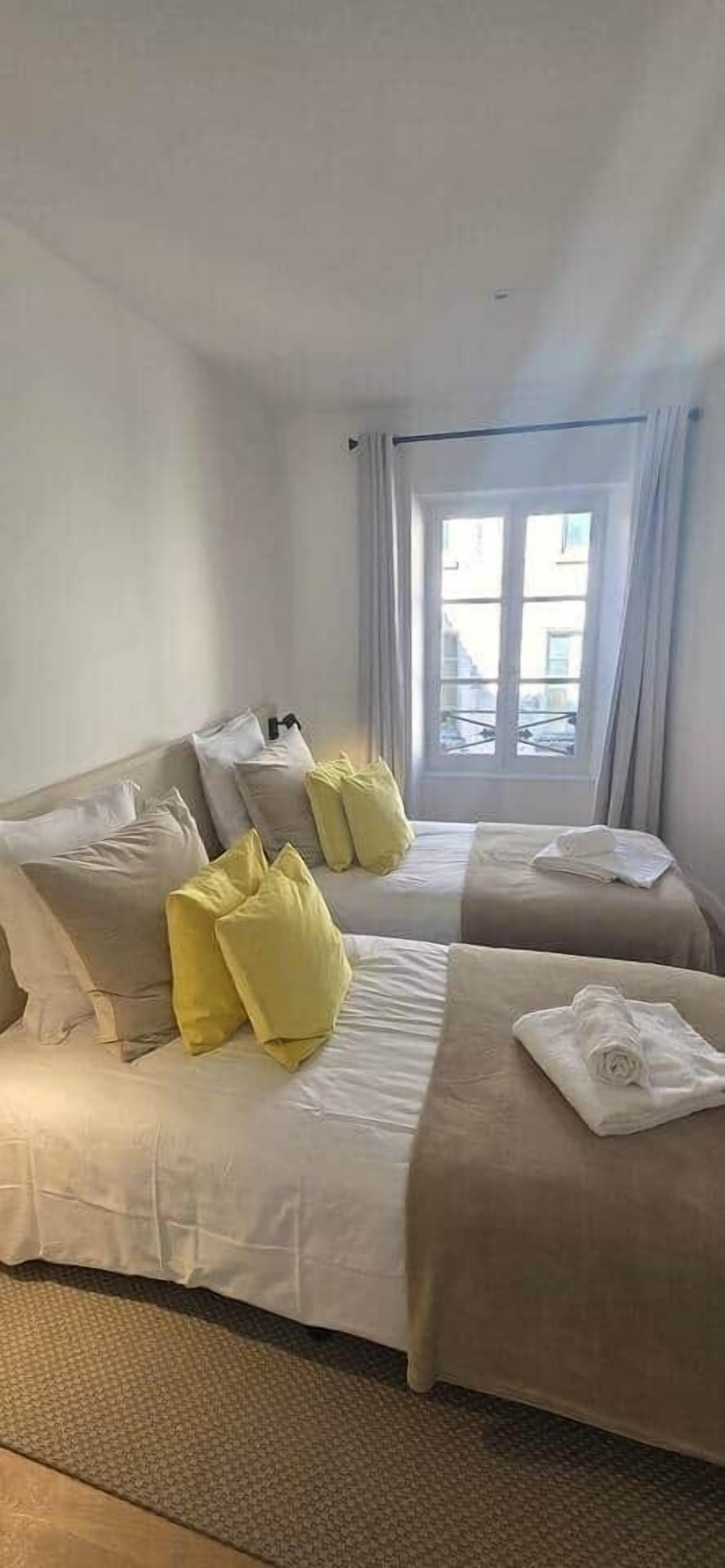 Quarto de hotel com duas camas, uma janela com cortinas e vista para prédios.
