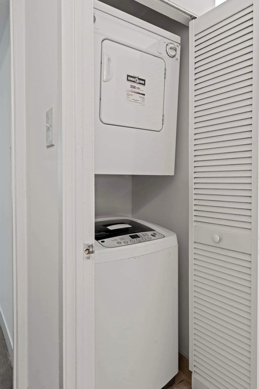 A compact laundry room with a front-loading washer and dryer, a visible energy efficiency label, and a white exterior wall.