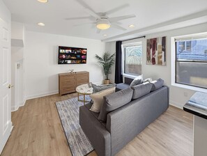 A modern living room with a grey sofa, a wooden cabinet, a ceiling fan, and a large TV mounted on the wall. - Fine Metro Oasis: 2BR Fits 6 Guests Near Landmarks (Philadelphia)