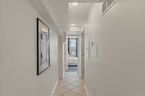 Un couloir avec un sol carrelé, des murs blancs et une porte donnant sur un balcon.