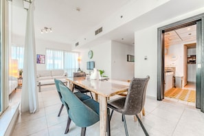 A modern living room with a sofa, a dining table with chairs, and a kitchen visible through an open doorway. - HAVN - 1 bedroom in Dubai Marina with Marina Views (Dubai)