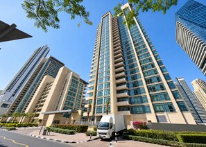 A high-rise building with multiple floors, a truck parked in front, and a clear blue sky. - HAVN - 1 bedroom in Dubai Marina with Marina Views (Dubai)