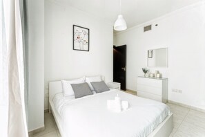 A modern bedroom with a bed, bedside tables, a dresser, a mirror, and a framed artwork on the wall. - HAVN - 1 bedroom in Dubai Marina with Marina Views (Dubai)