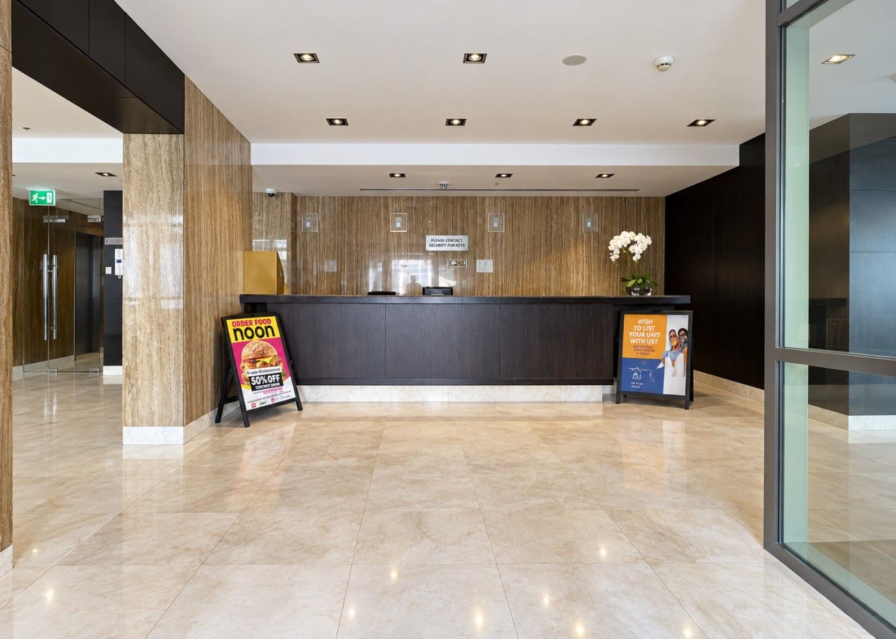 Zona de recepción de un hotel con suelo de mármol, mostrador de recepción y carteles que anuncian comida y un descuento.